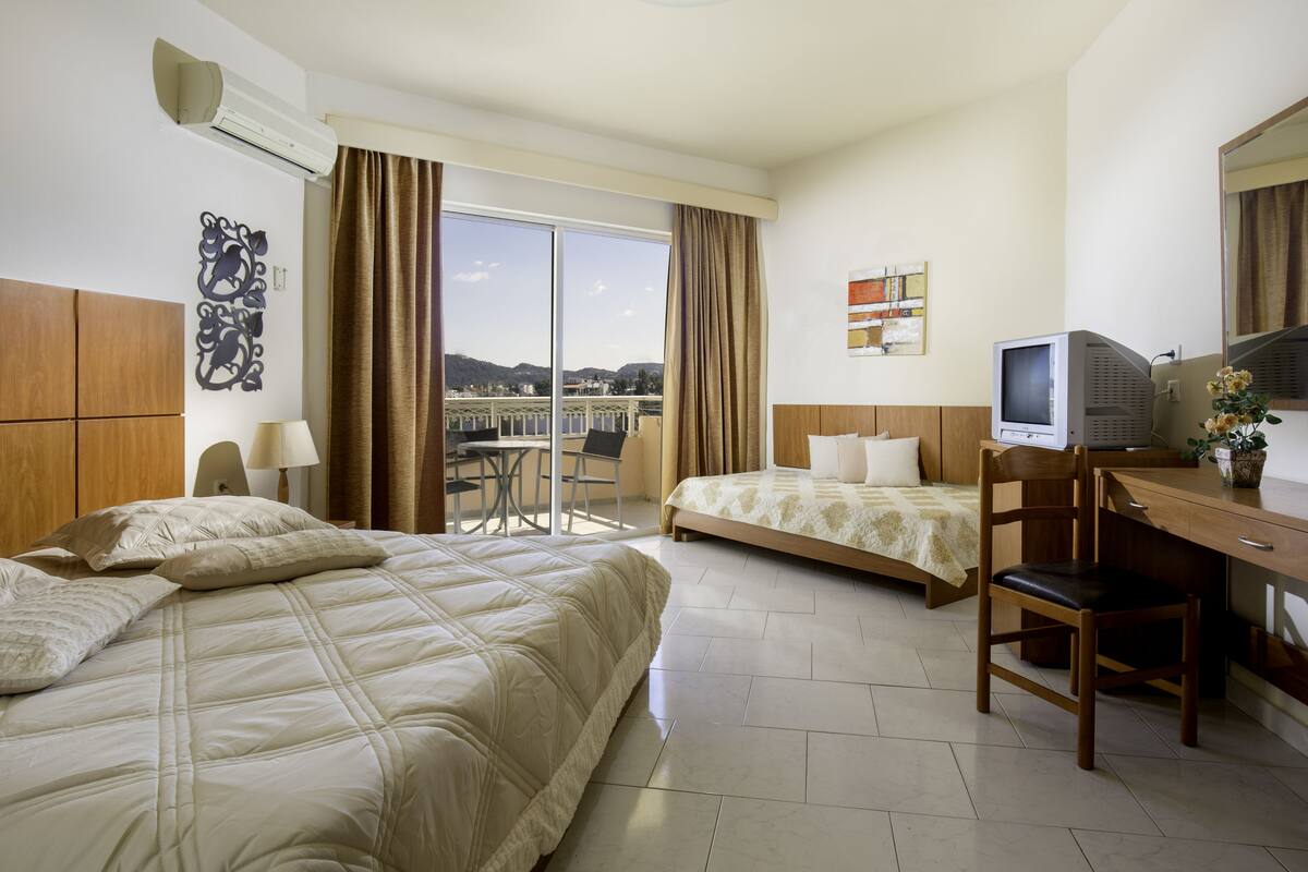 Une chambre d’hôtel avec deux lits, un bureau avec une télévision et une vue sur un pont et des montagnes.