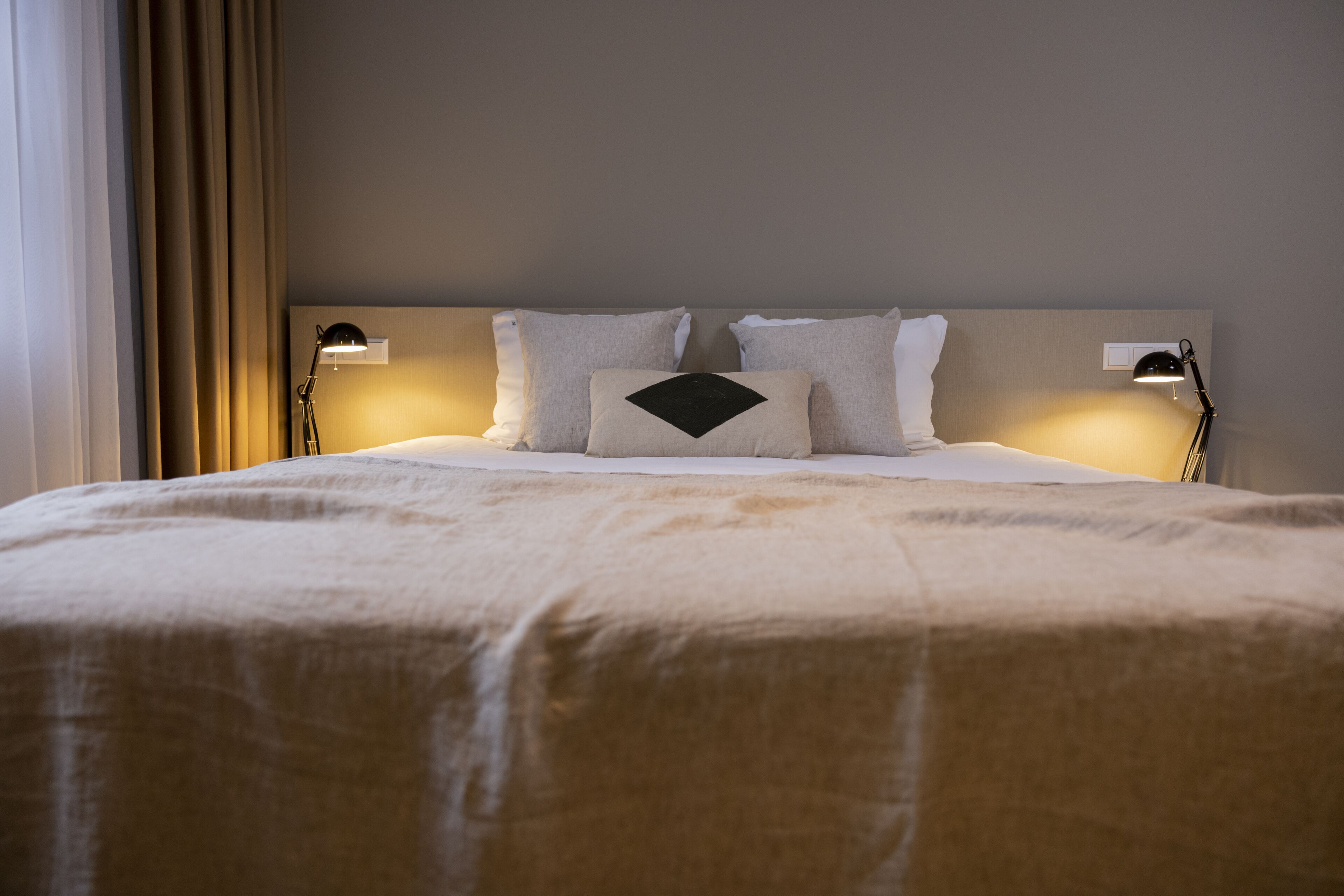 Una cama bien hecha con un edredón color beige y dos almohadas, con dos lámparas de noche a cada lado.