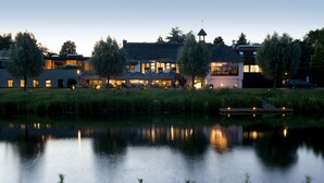 A lakeside hotel with a dining area, outdoor seating, and a reflection in the water. - Hotel Mooirivier (Dalfsen)