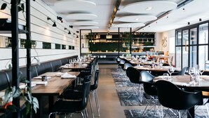 A modern restaurant with long tables, black chairs, and a central bar area. - Hotel Mooirivier (Dalfsen)