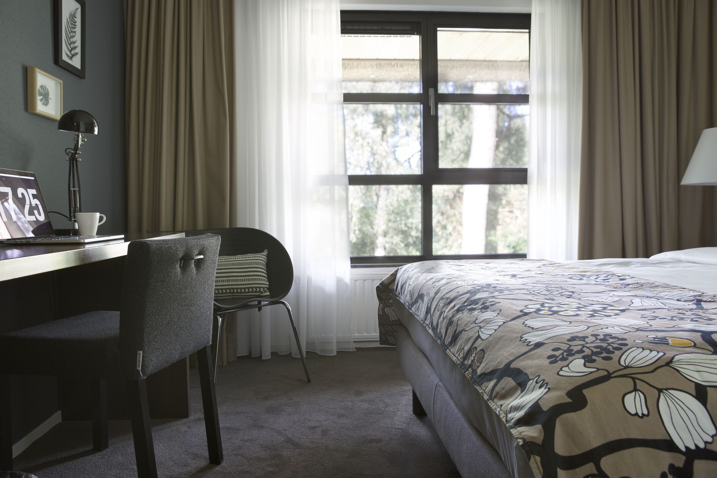 Una camera d'albergo con un letto, una scrivania, una sedia e una finestra con tende.