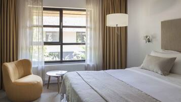 Una camera d'albergo con un letto, una sedia, un tavolino, una lampada e una finestra con tende.