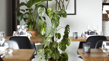 Un comedor con mesas de madera, plantas en macetas y cuadros en la pared.