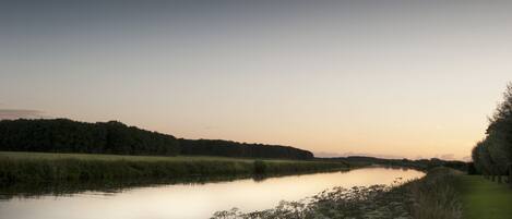 A calm river with a grassy bank and trees in the background.