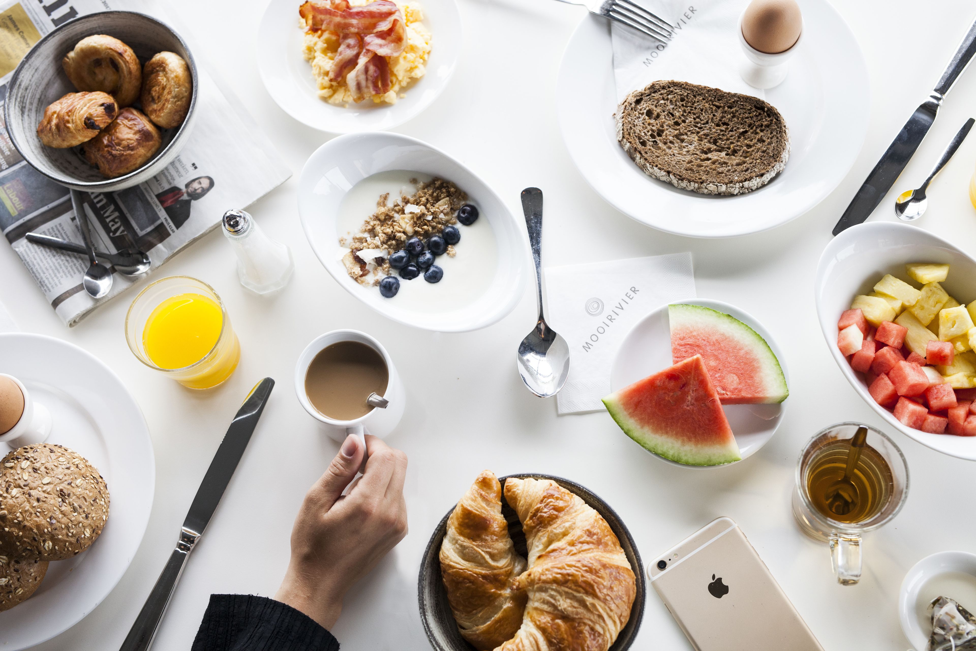 Een ontbijttafel met croissants, roerei, toast en diverse soorten fruit en drankjes.