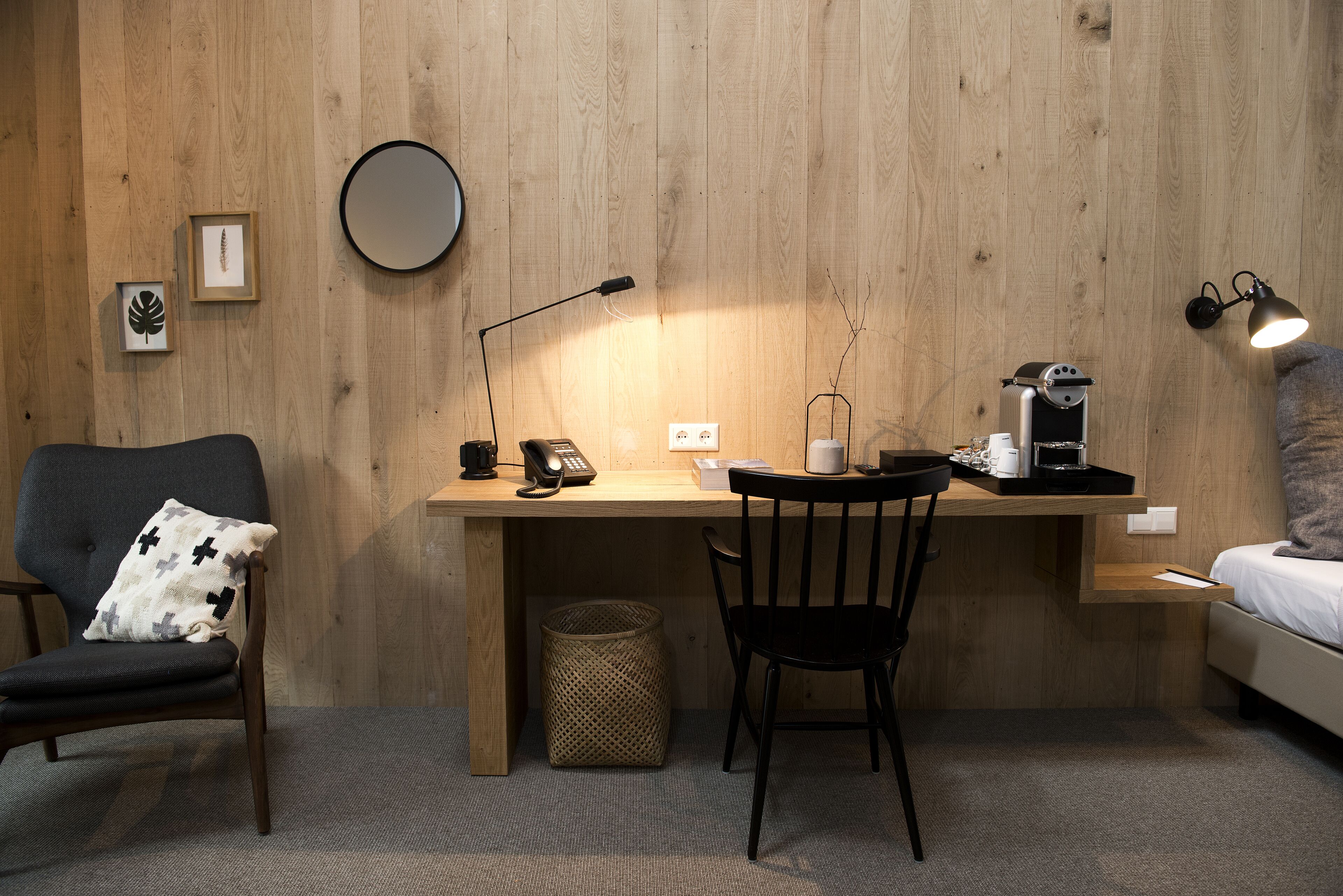A compact room with a wooden desk, a chair, a bed, and a small side table.