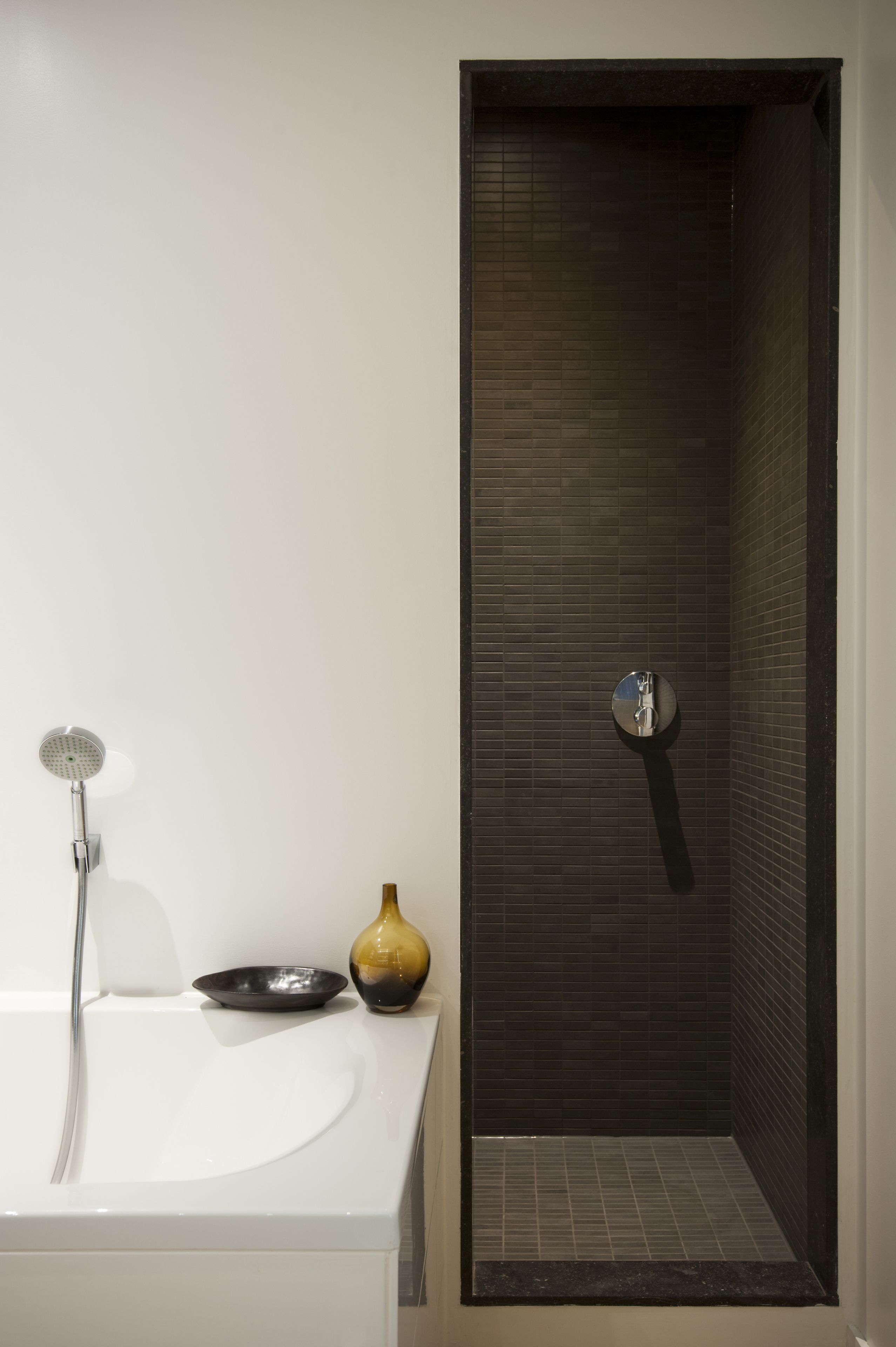 A modern bathroom with a white sink, a shower with a dark tiled wall, and a small decorative vase.