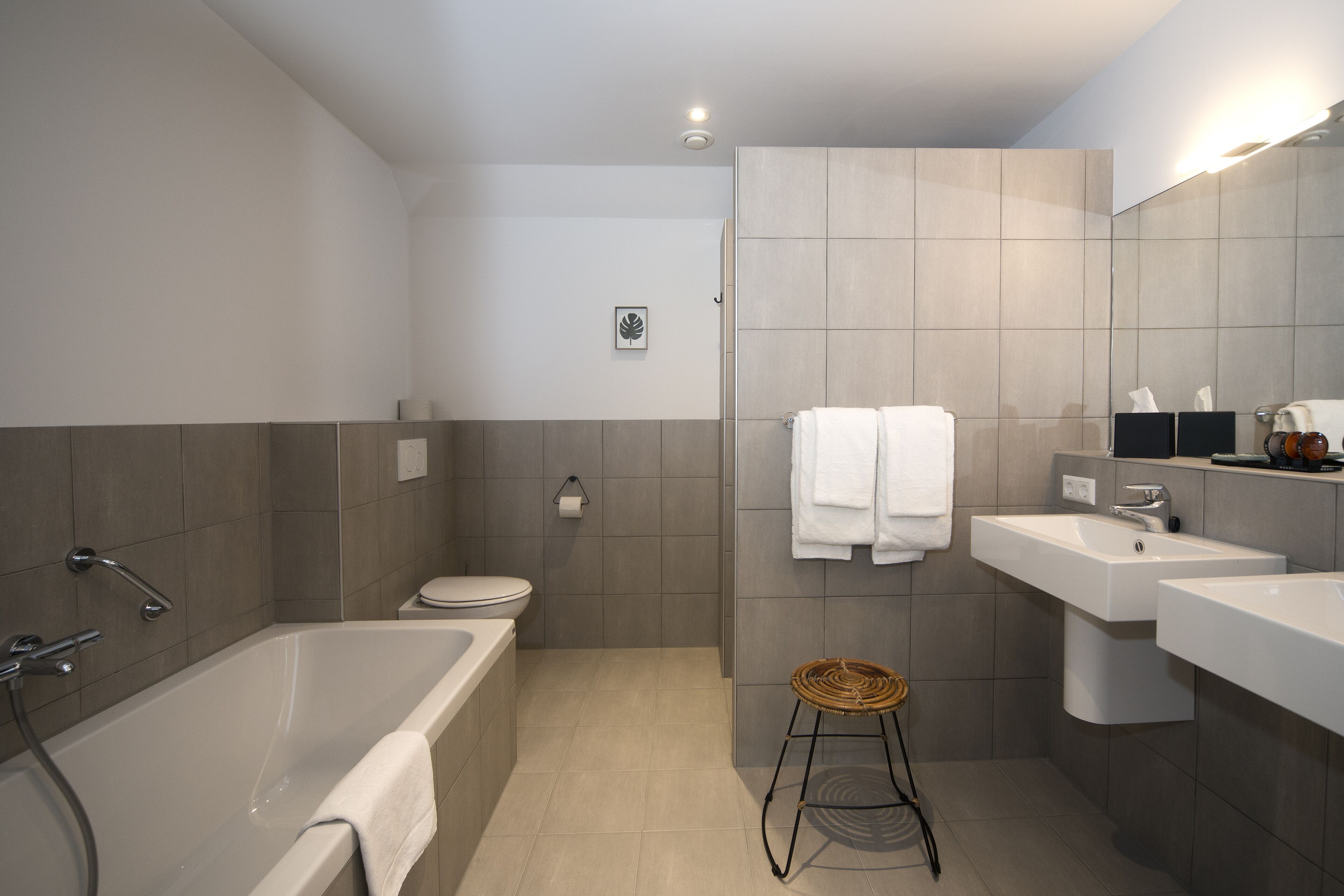 A modern bathroom with a bathtub, toilet, and two sinks.