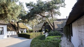 A traditional building with a thatched roof, surrounded by well-maintained hedges and trees. - Hotel Mooirivier (Dalfsen)