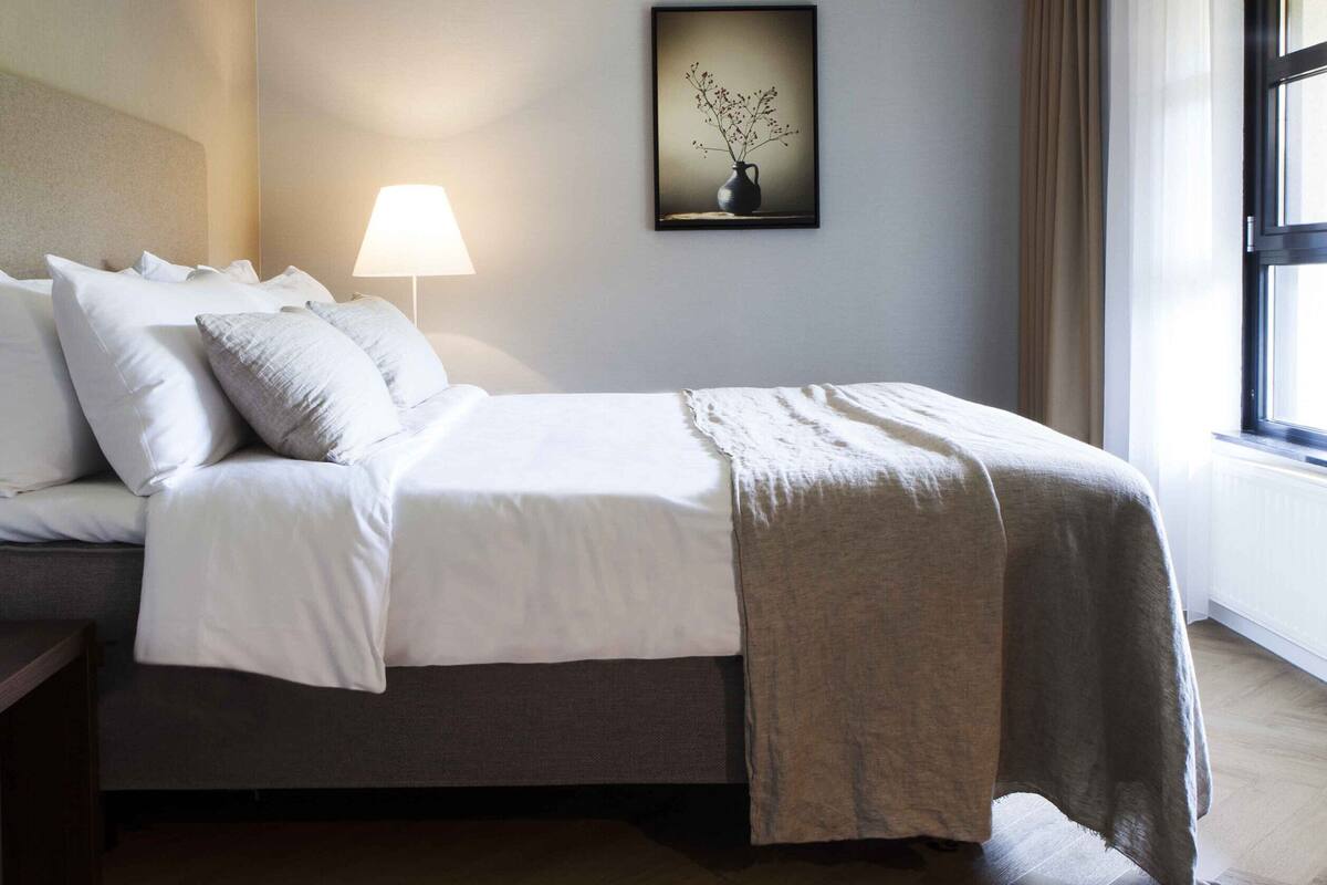 A modern bedroom with a bed, bedside table, lamp, and a framed picture on the wall.