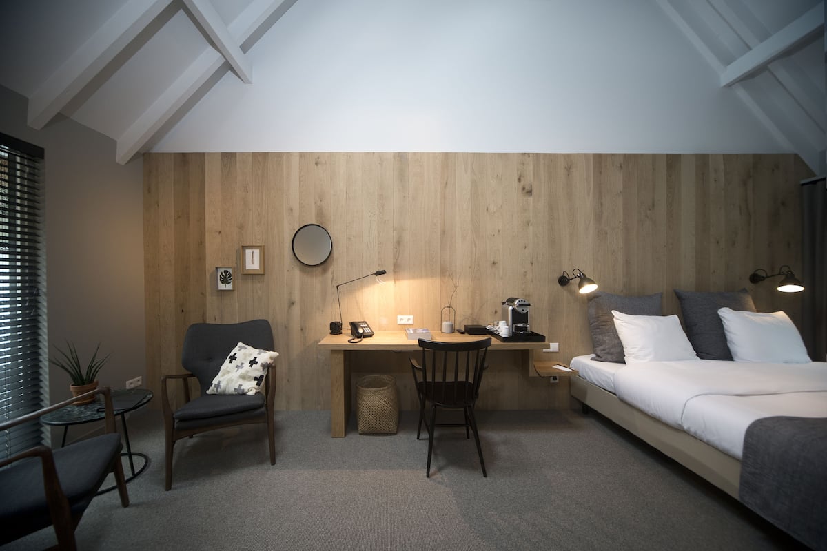 A compact room with a wooden accent wall, a desk with a chair, a bed, and a small table with a plant.
