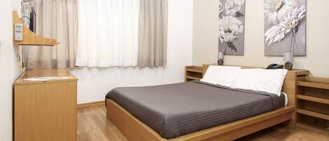 Un dormitorio moderno con una cama de madera, mesitas de noche, un escritorio y dos cuadros colgados en la pared.
