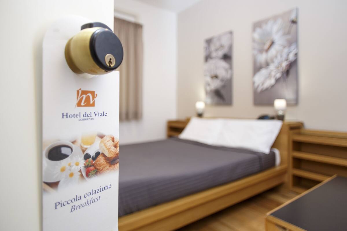 A hotel room with a bed, a wooden headboard, a small table, and a wall-mounted keycard holder.