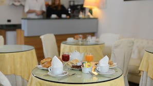 A breakfast setting with tables, chairs, and a counter in the background. - Albergo Italia (Matera)
