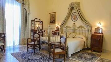 Quarto com cama de dossel, duas cadeiras de madeira, uma mesa de cabeceira e um espelho.