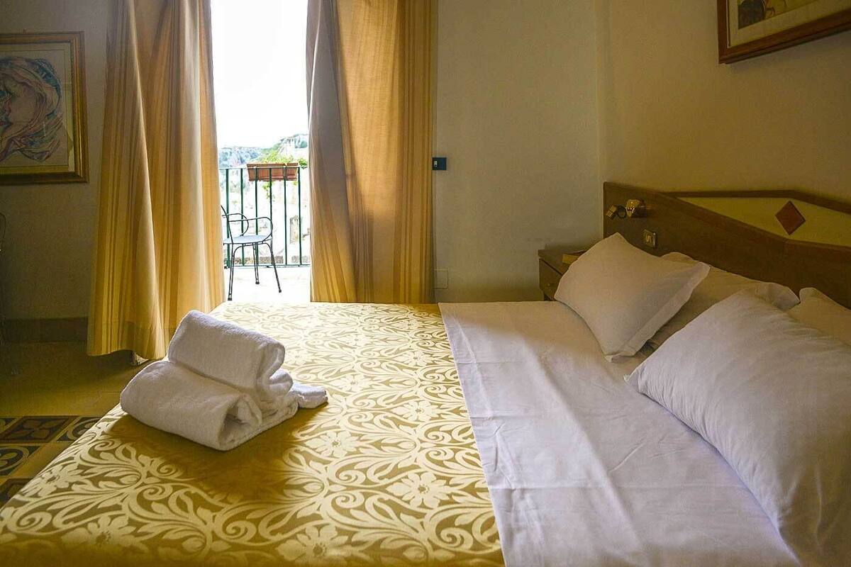 Habitación de hotel con una cama, una mesita de noche y vistas al exterior.