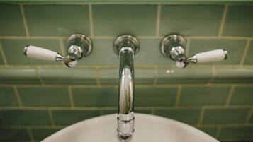 A bathroom with a white sink, green tiled walls, and three chrome faucets with white handles.