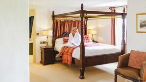 A four-poster bed with a wooden frame, a nightstand with a lamp, and a chair with a cushion.