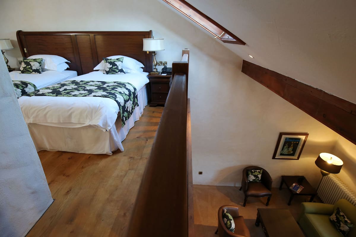Une chambre avec deux lits, un banc en bois, une petite table, une chaise et une lampe.