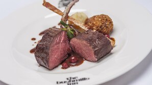 A plate with a lamb chop, a piece of bread, and a small round item, possibly a side dish.