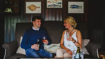 A couple sitting on a couch in a room with wooden paneling and framed fish artwork on the wall.
