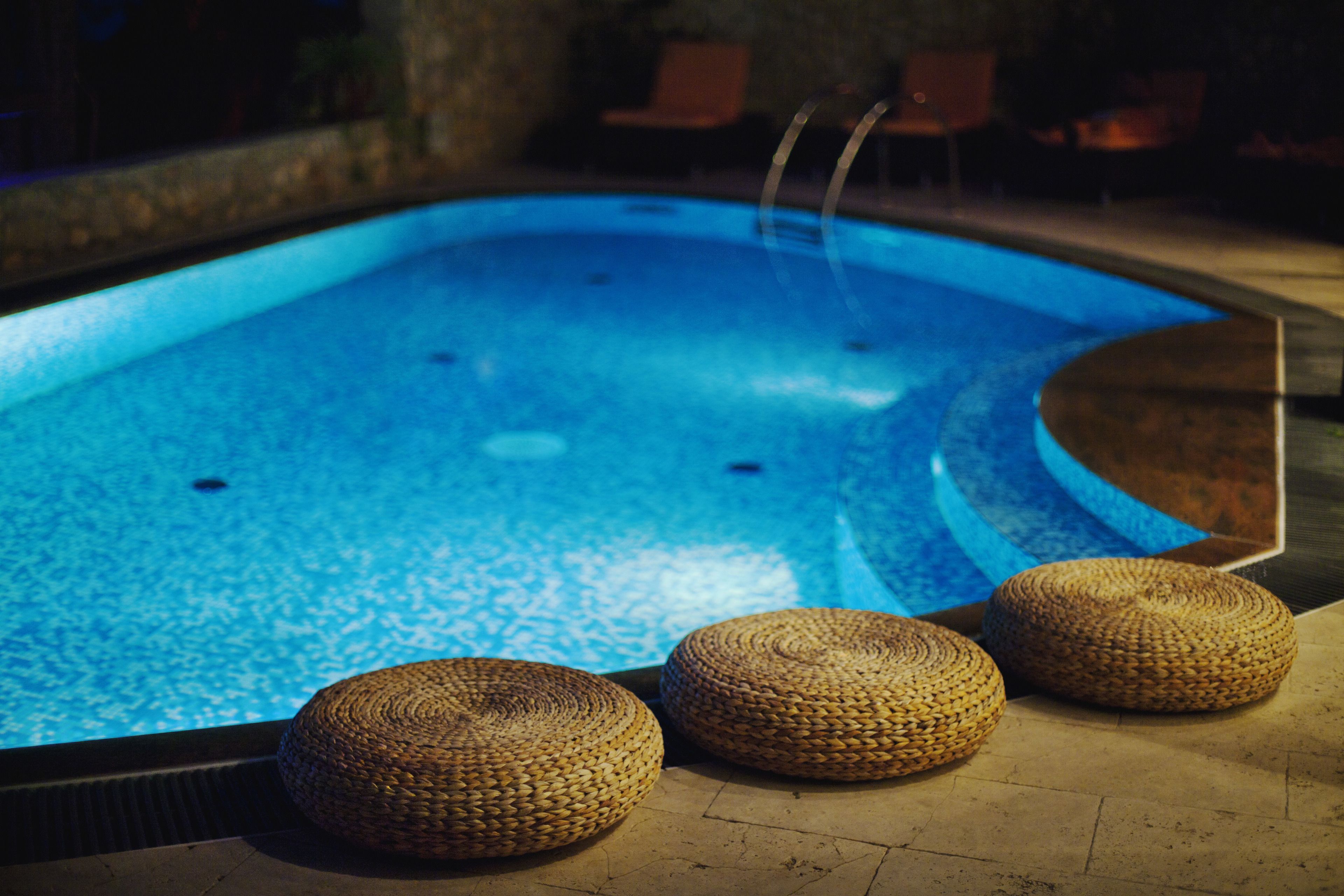 Une piscine avec trois tabourets en osier au premier plan.