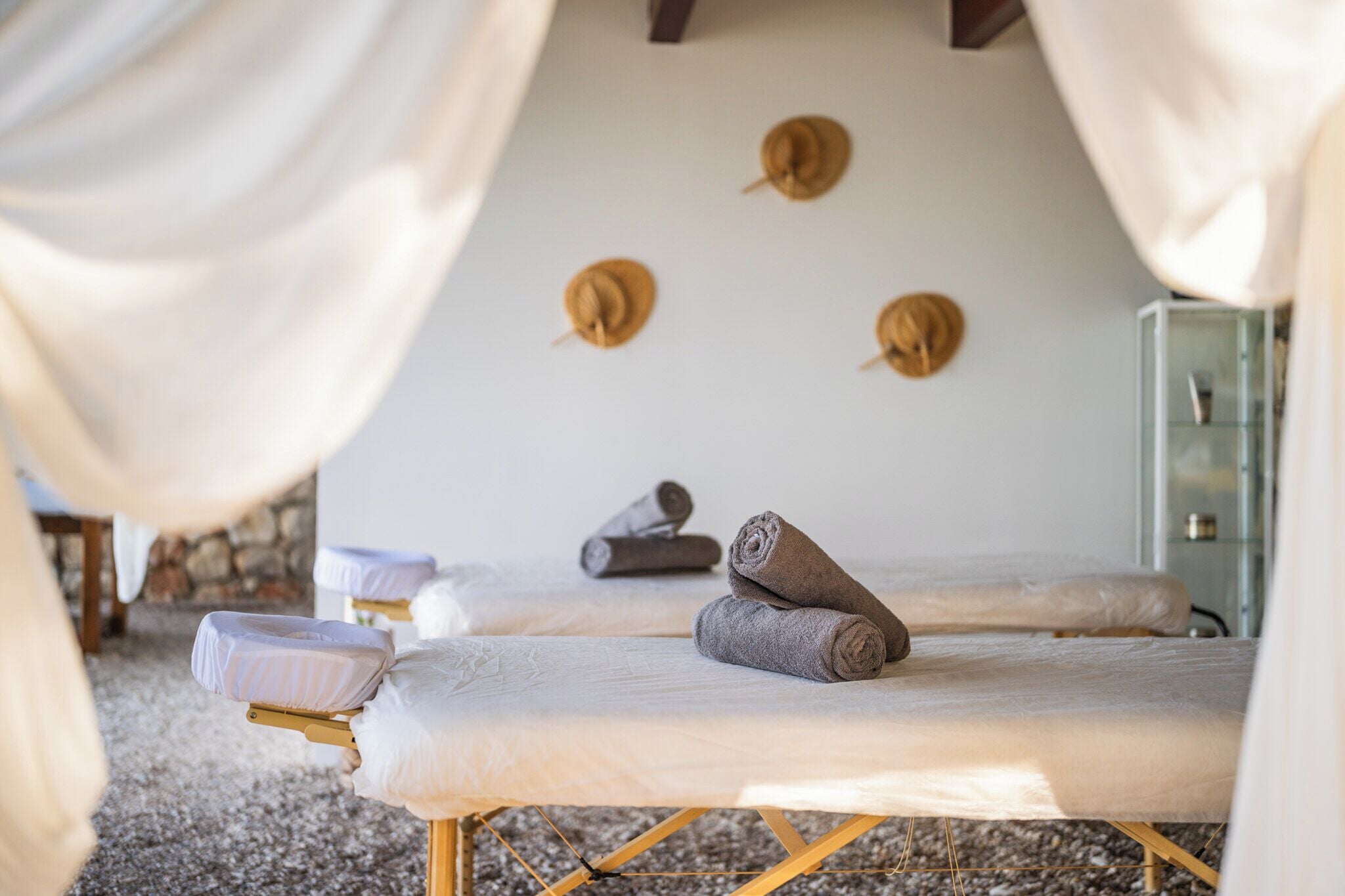 A spa room with two massage tables, towels, and a glass cabinet.
