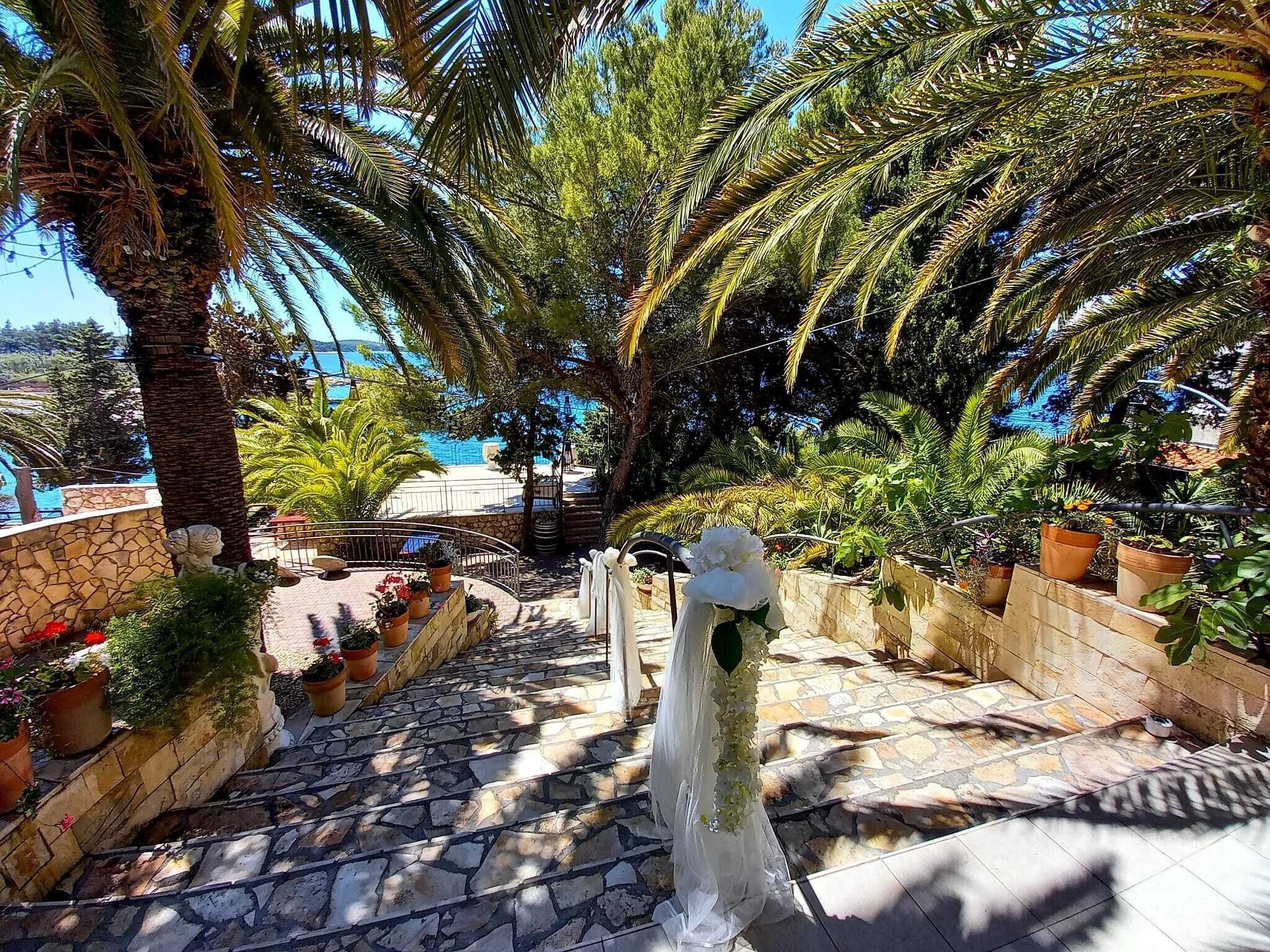 Un escalier en pierre mène à une terrasse agrémentée de plantes en pot et offrant une vue sur la mer.
