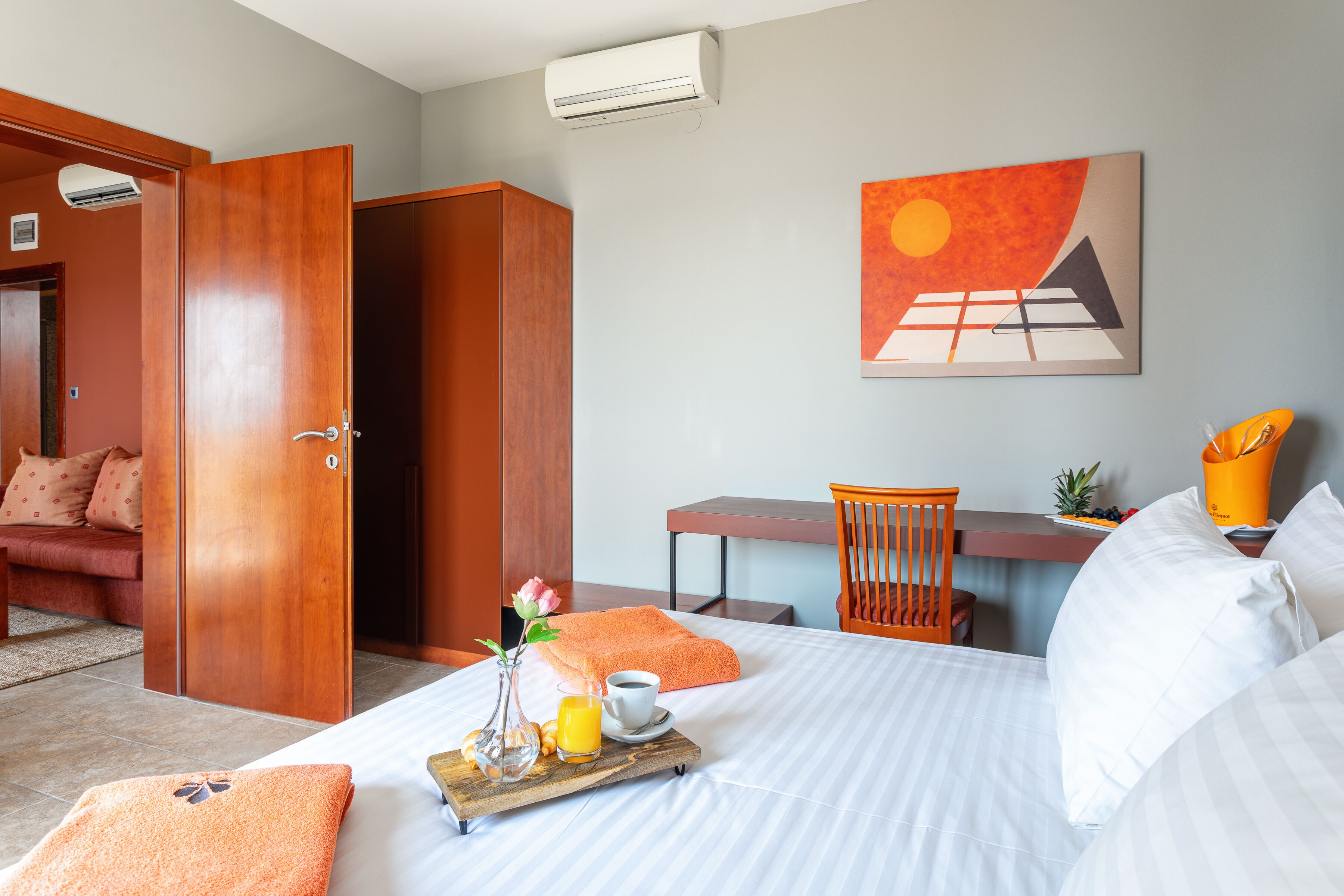 A hotel room with a bed, a desk, a chair, and a painting on the wall.
