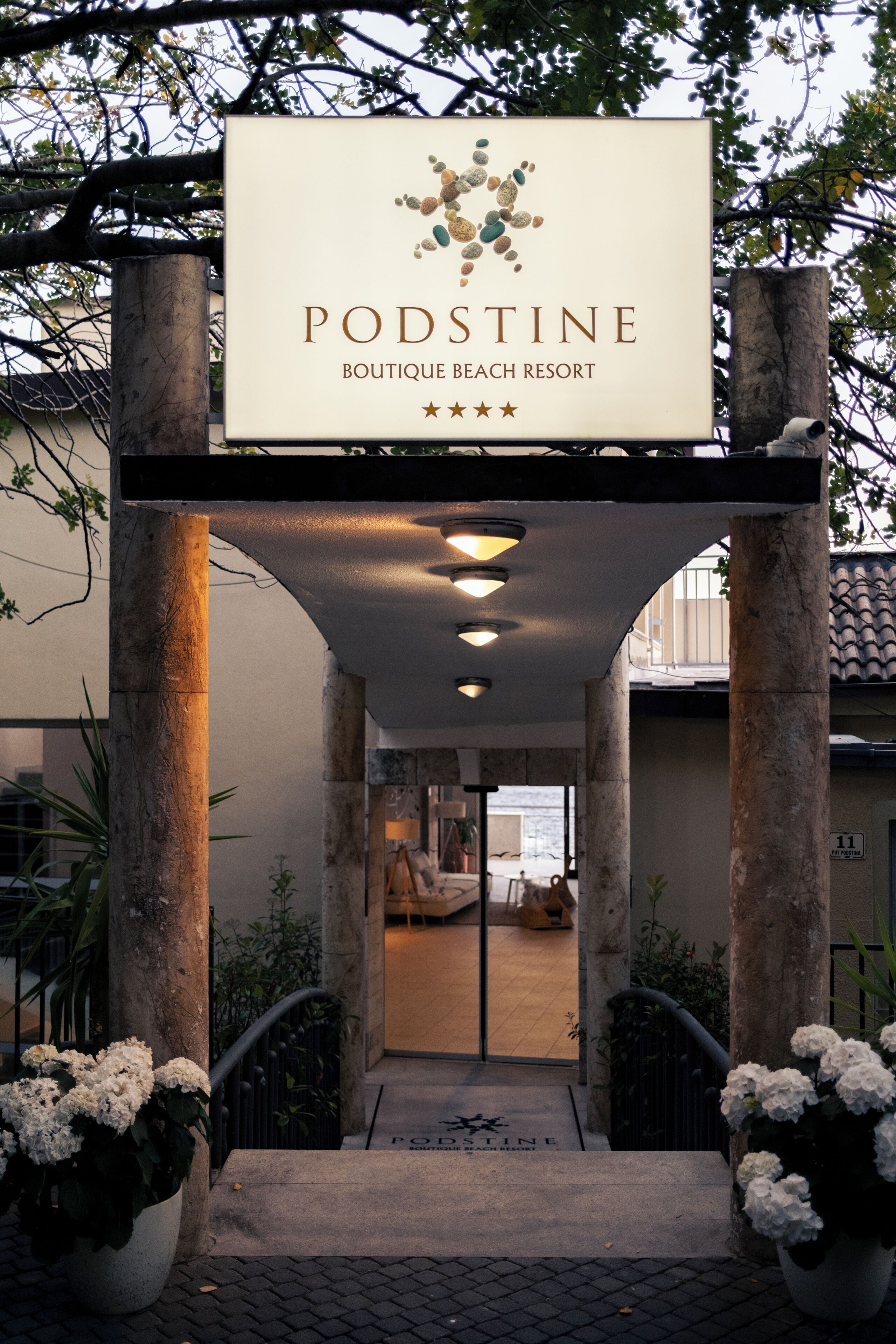 A sign for Podstine Boutique Beach Resort with a clear entrance and potted plants.