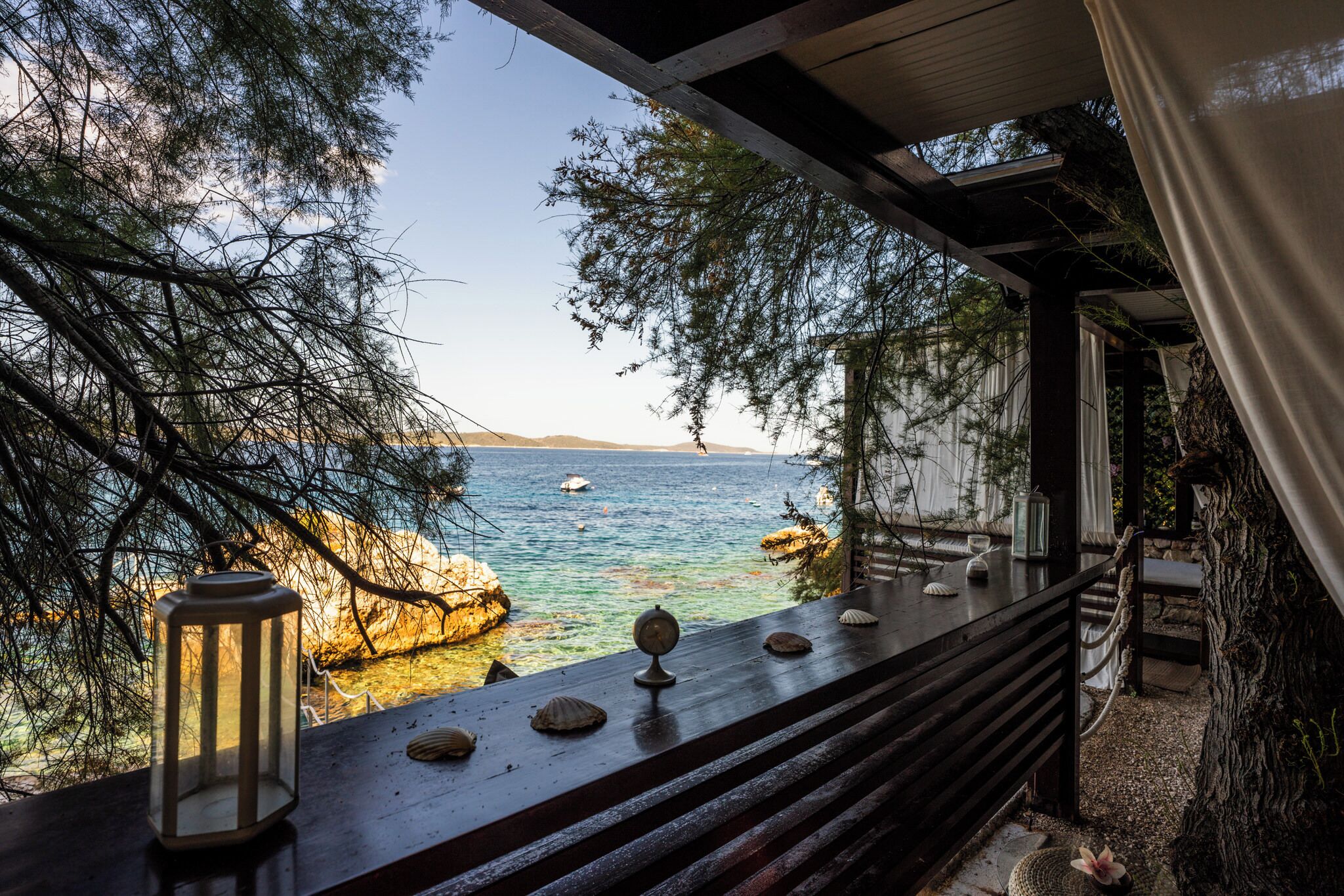 A coastal view from a wooden deck with a lantern, seashells, and a rustic railing.