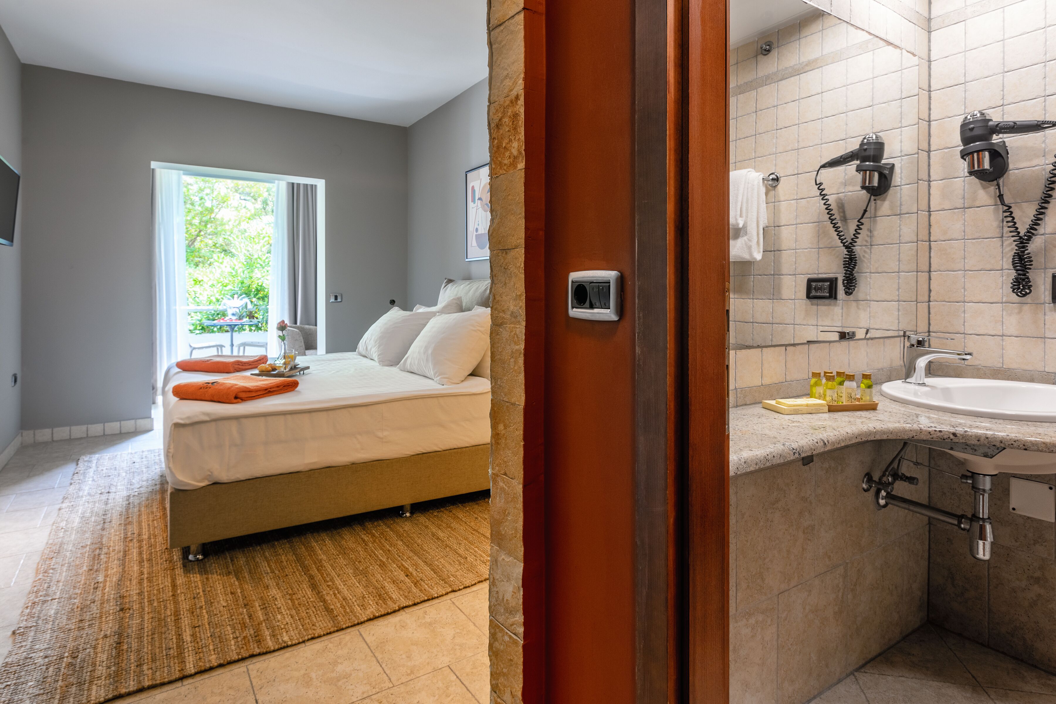 Habitación de hotel con cama, baño con lavamanos y secador de pelo, y vista a zonas verdes.