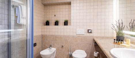A bathroom with a glass shower enclosure, a bidet, a toilet, and a sink with a marble countertop.