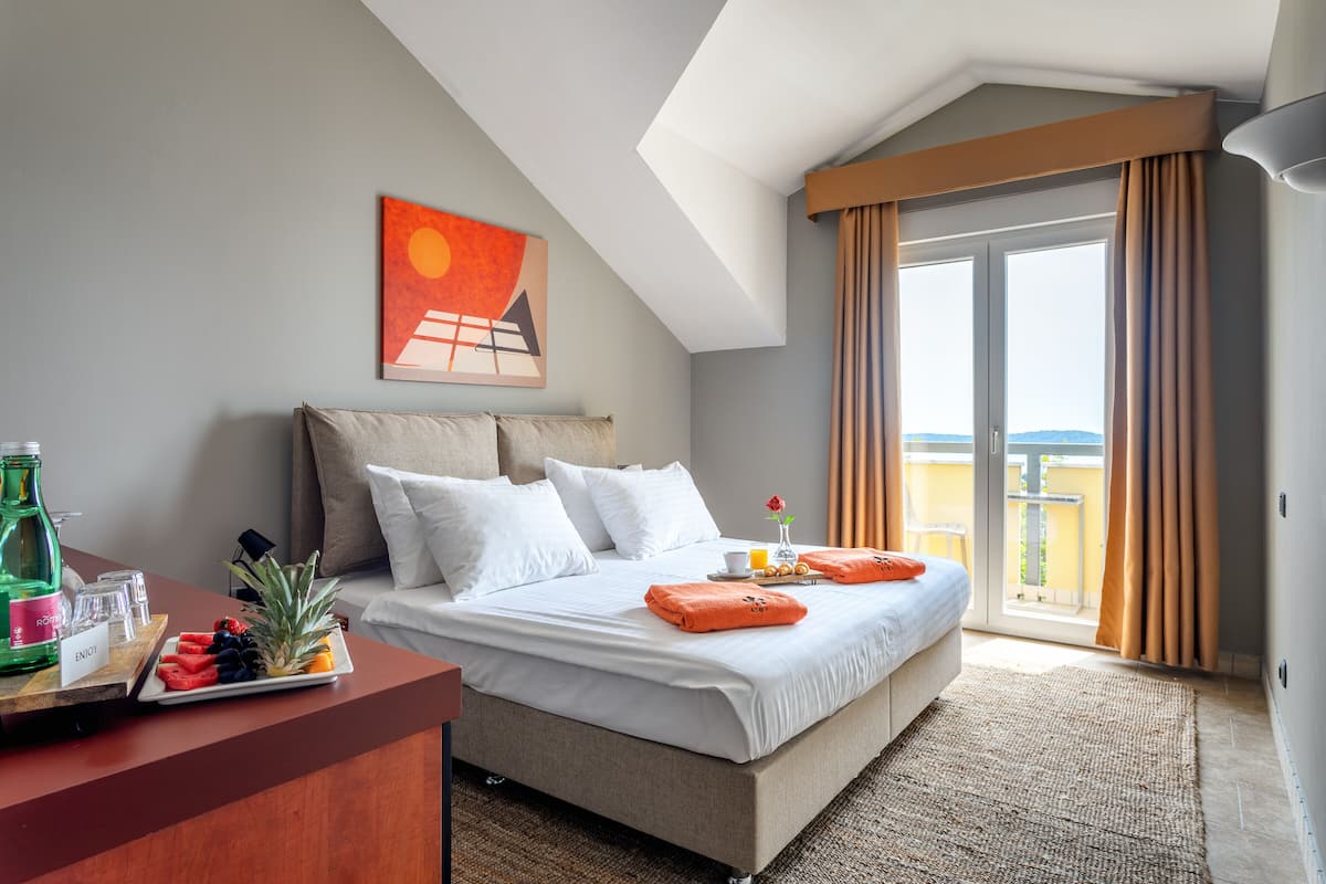 A hotel room with a bed, a breakfast tray, a bottle of water, and a painting on the wall.