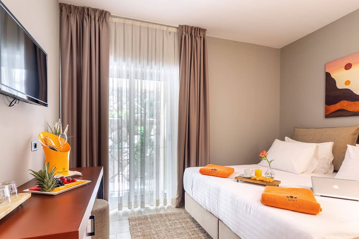 A hotel room with a bed, a desk with a fruit platter, a laptop, and a painting on the wall.