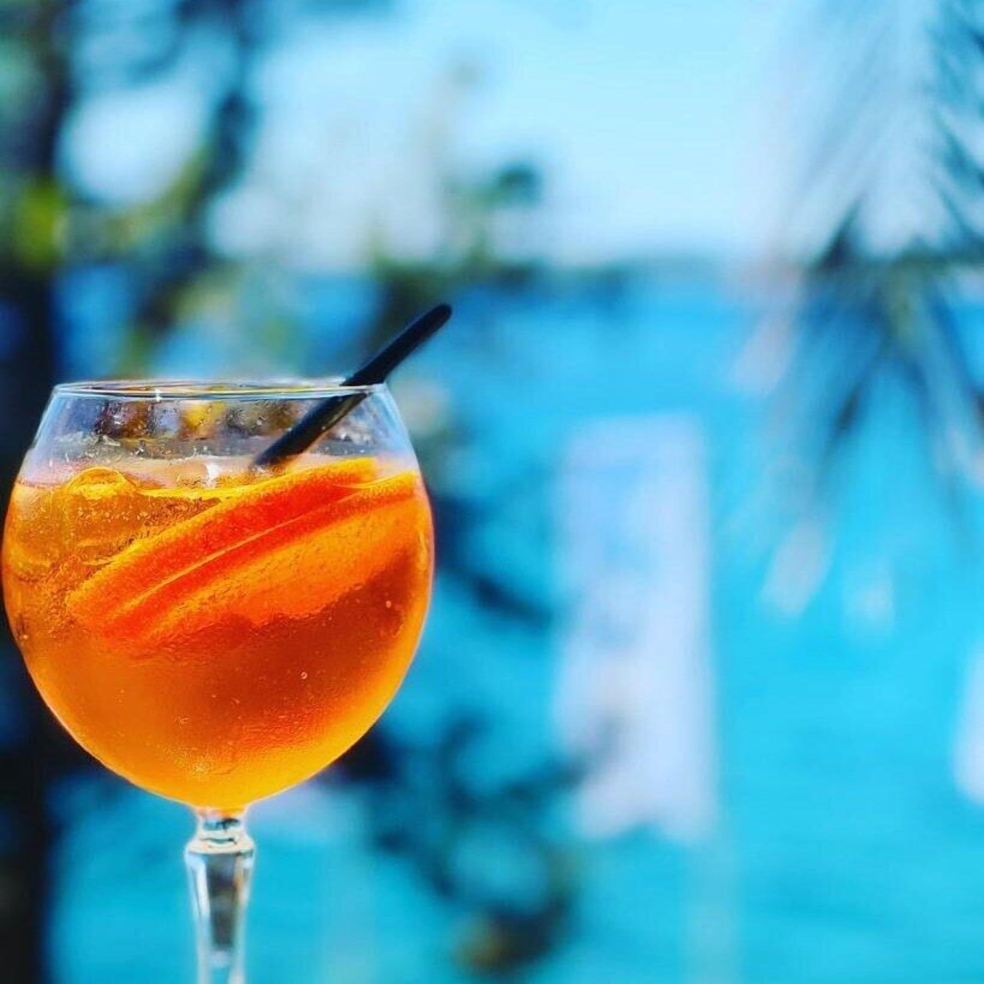 A cocktail glass with a straw, containing a clear liquid and orange garnish, set against a blurred blue background.