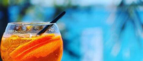 A cocktail glass with a straw, containing a clear liquid and orange garnish, set against a blurred blue background.