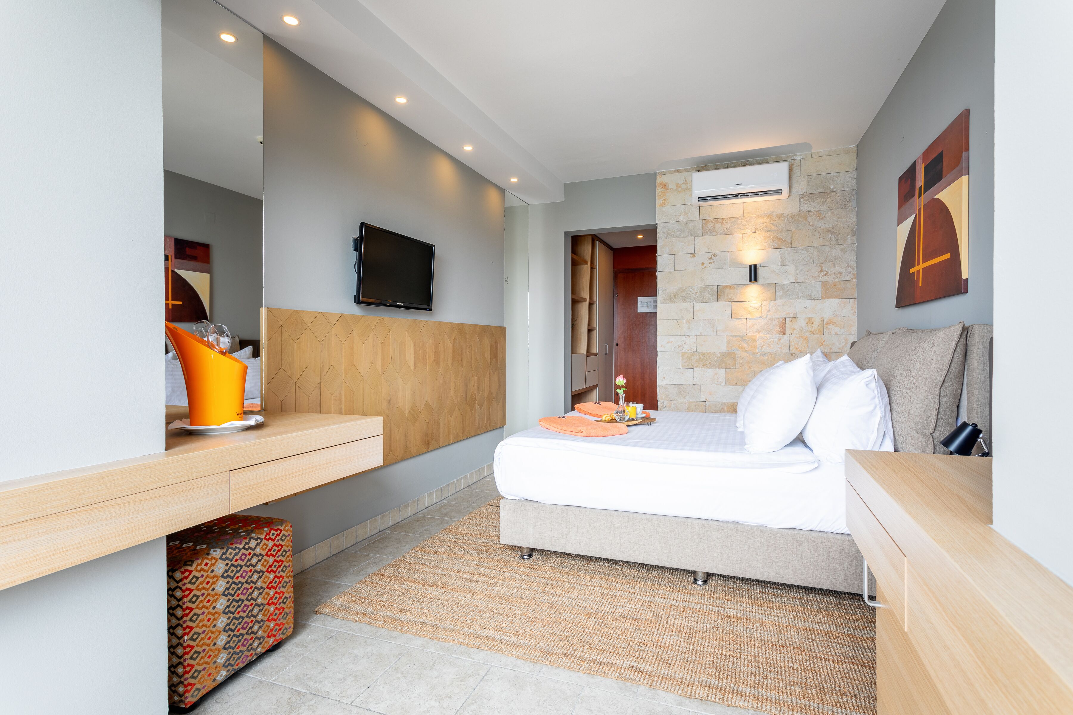 A modern hotel room with a bed, bedside table, TV, and a stone accent wall.