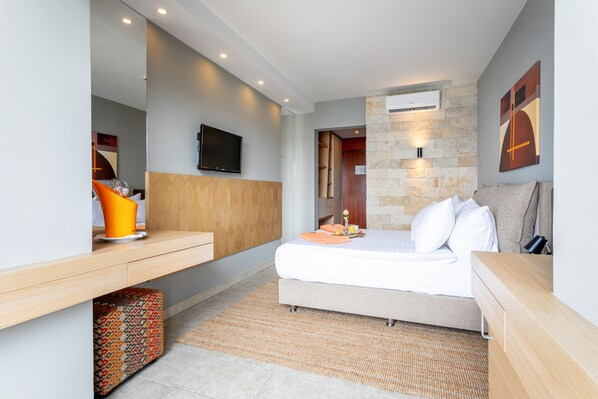 Habitación de hotel moderna con cama, mesita de noche, televisor y una pared de detalles de piedra.
