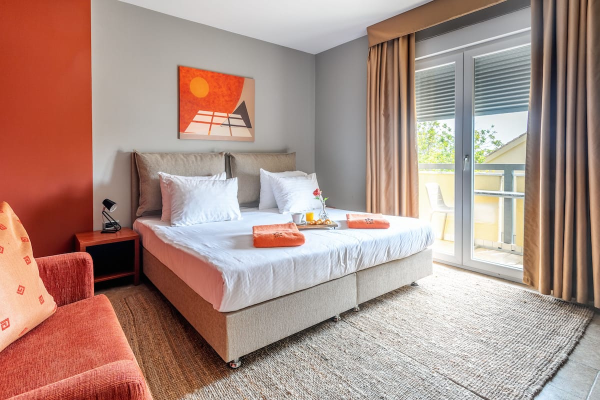 A hotel room with a large bed, a nightstand, a chair, and a balcony with a view.
