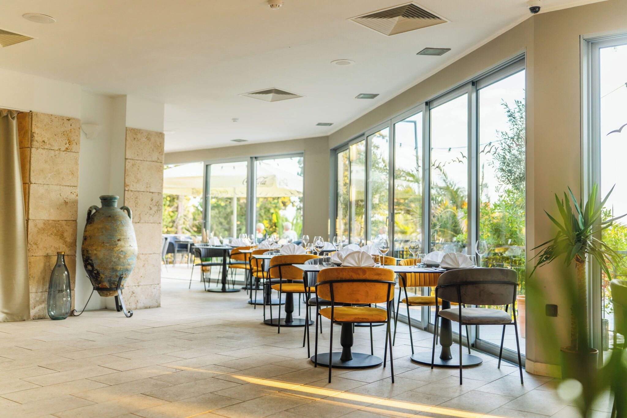 Ein Restaurant mit Tischen, Stühlen, großen Fenstern und einem Fliesenboden.