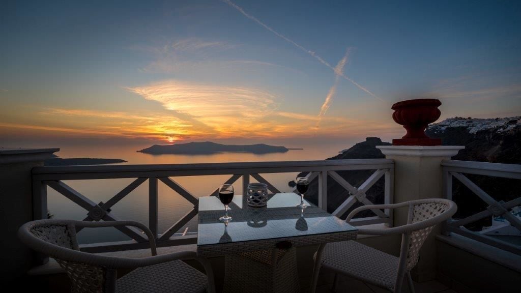 A terrace with a table and chairs overlooking a sunset view.