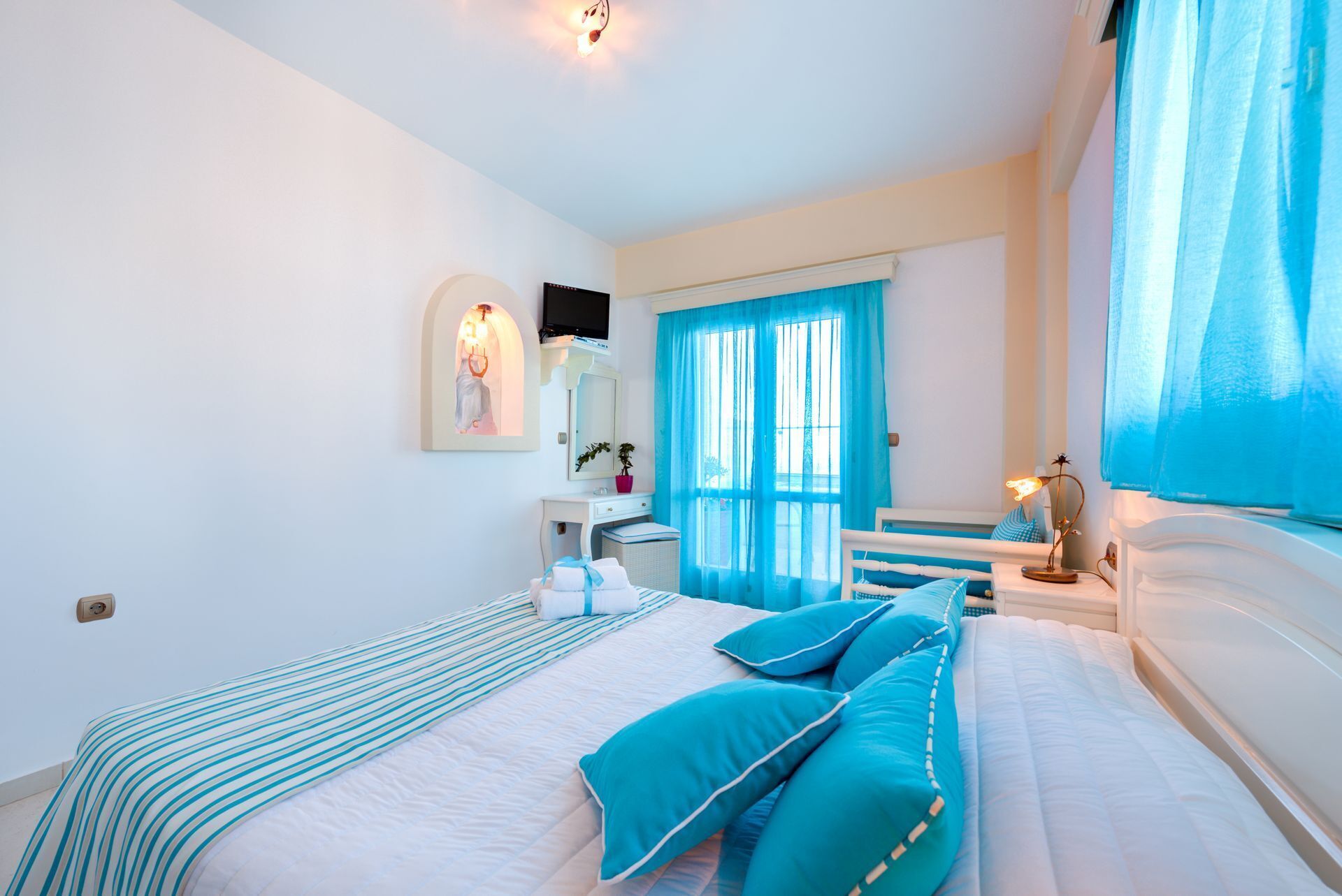 Een slaapkamer met een groot bed, een nachtkastje, een spiegel en een raam met blauwe gordijnen.