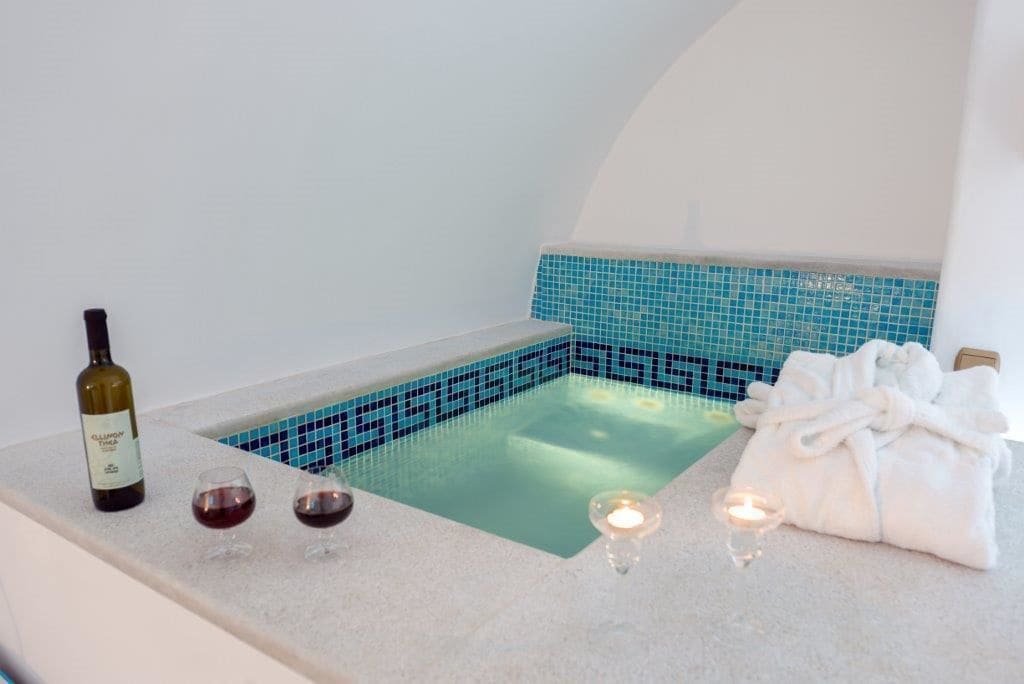 A spa area with a bathtub, a bottle of wine, and two glasses on a counter.
