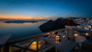 A terrace with a table and chairs, overlooking a coastal town at dusk.
