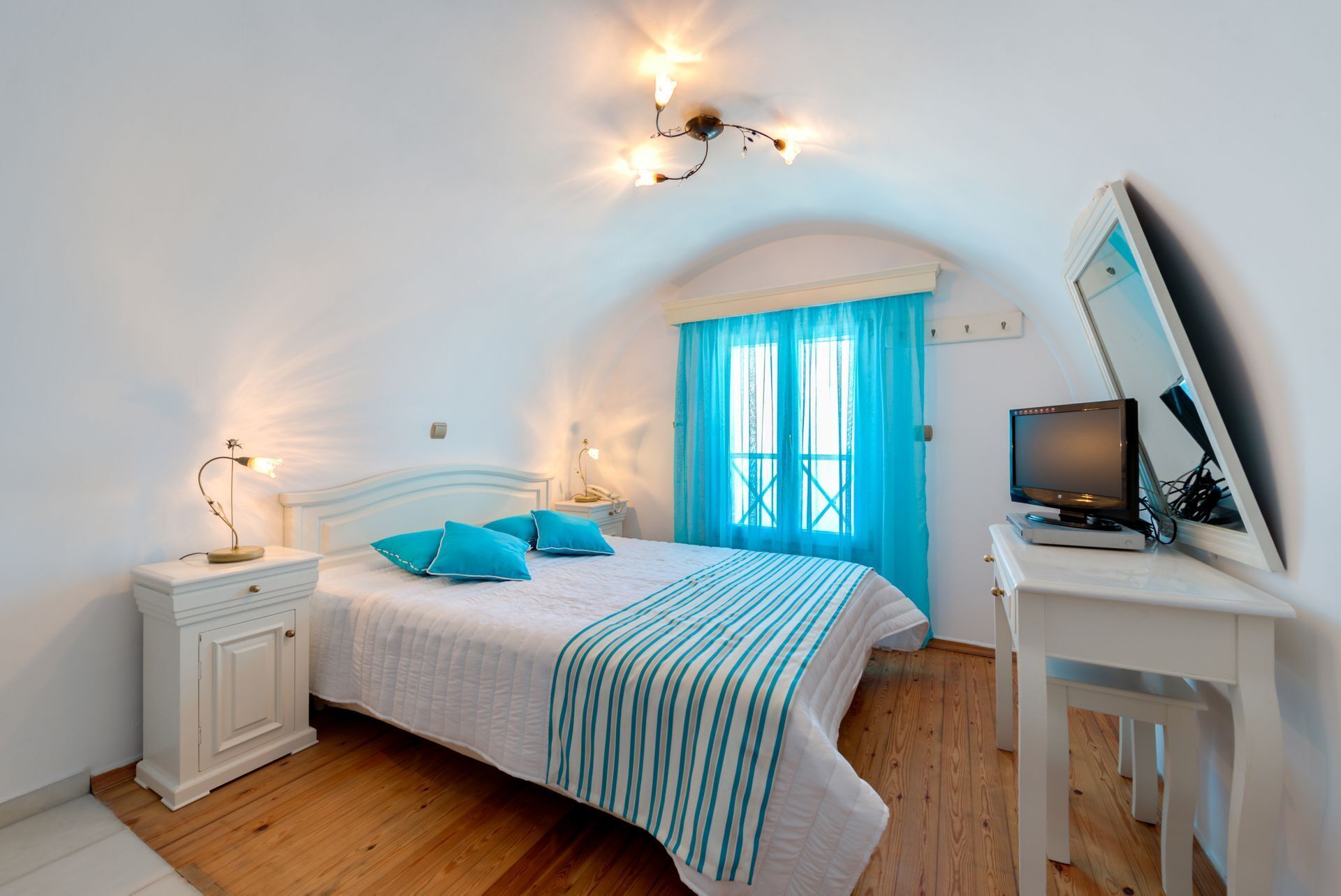 A bedroom with a bed, bedside tables, a desk with a computer, and a window with curtains.