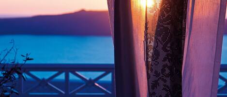 A balcony with a view of the sea and distant mountains at sunset.