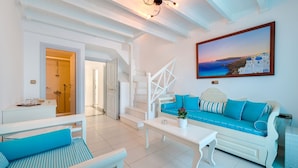 A bright, white room with a sofa, a coffee table, and a painting of a coastal scene.