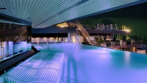 Un área de piscina interior moderna con una barrera de cristal, una escalera y un balcón con vistas a un paisaje verde.
