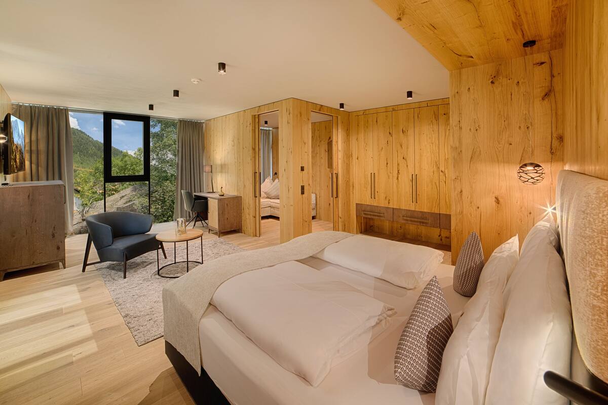 A modern bedroom with a large bed, wooden panel walls, a desk, and a chair.
